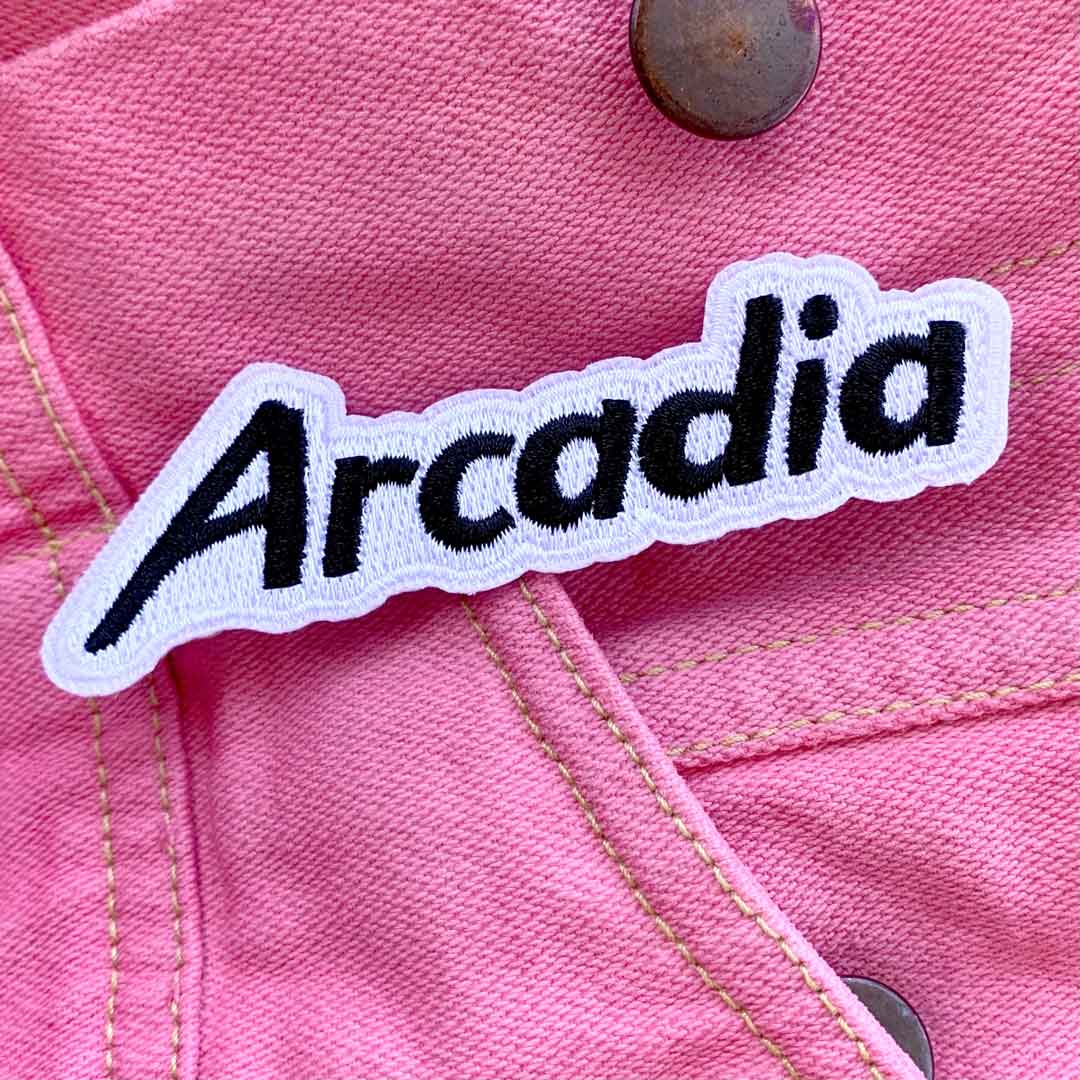 Arcadia album art: a fabric patch reading "ARCADIA" over a pink denim jacket